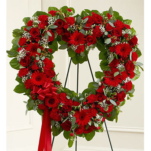 A heart shaped wreath of red roses and greenery.