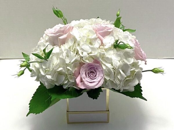 A white and pink flower arrangement in a square vase.