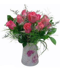 A vase filled with pink roses and greenery.