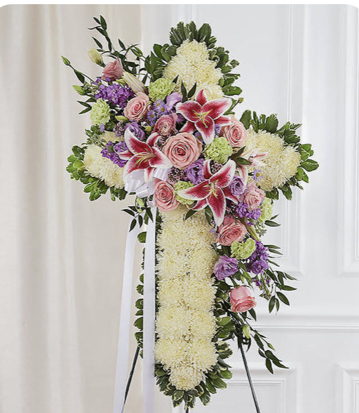 A cross of flowers with greenery and pink roses.