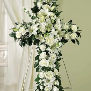 A cross of white flowers with greenery.