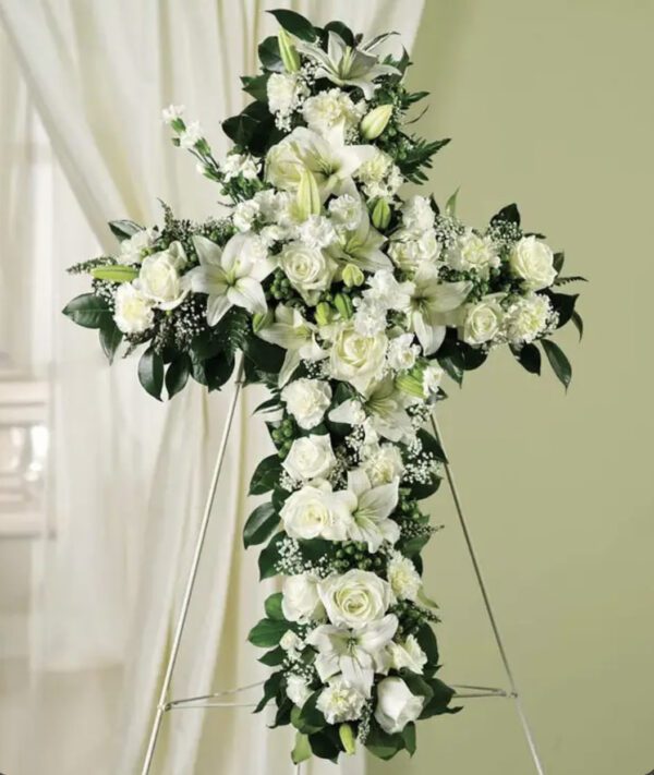 A cross of white flowers with greenery.