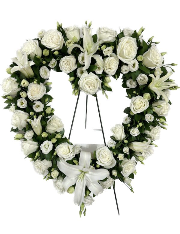 A heart shaped wreath of white flowers on a stand.