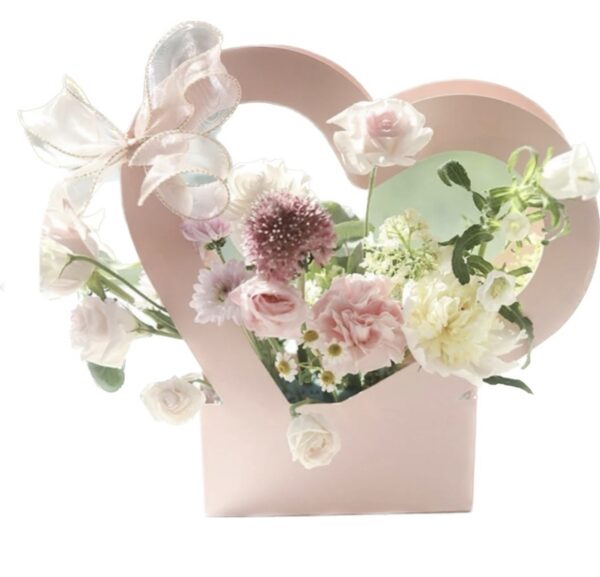 A pink heart shaped vase filled with flowers.